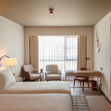 Epic Sana Marques Hotel Lissabon Exterior foto The photo depicts a modern hotel room featuring two beds with white linens. The room is well-lit, with large windows dressed in sheer curtains that allow natural light to filter in. There are two comfortable armchairs next to a small side table, prov