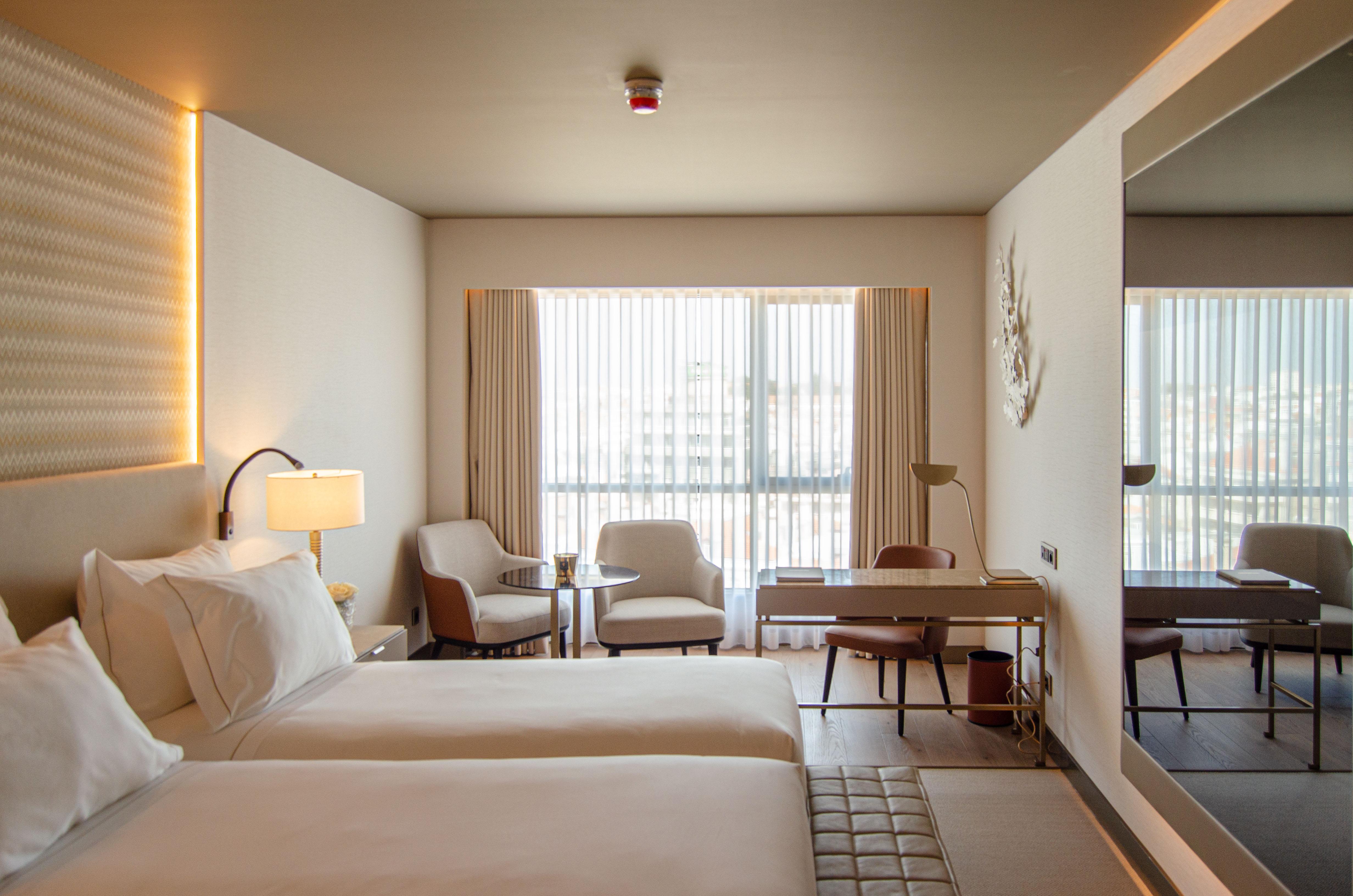 Epic Sana Marques Hotel Lissabon Exterior foto The photo depicts a modern hotel room featuring two beds with white linens. The room is well-lit, with large windows dressed in sheer curtains that allow natural light to filter in. There are two comfortable armchairs next to a small side table, prov