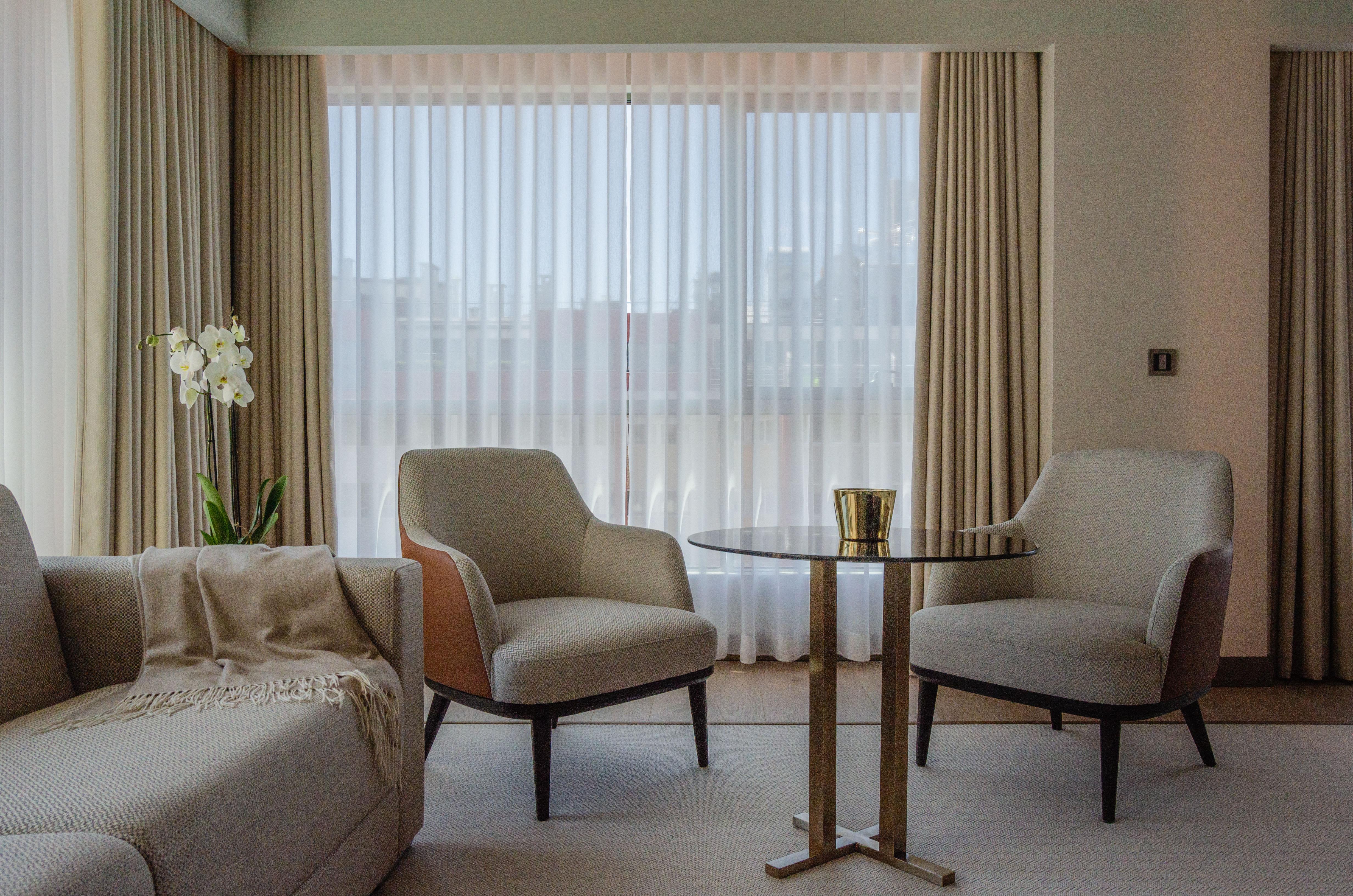 Epic Sana Marques Hotel Lissabon Exterior foto The photo shows a modern and stylish interior space, likely a living room or lounge area. There are two upholstered chairs positioned around a small round table. The chairs have light-colored upholstery with wooden accents. A light-colored sofa is pl