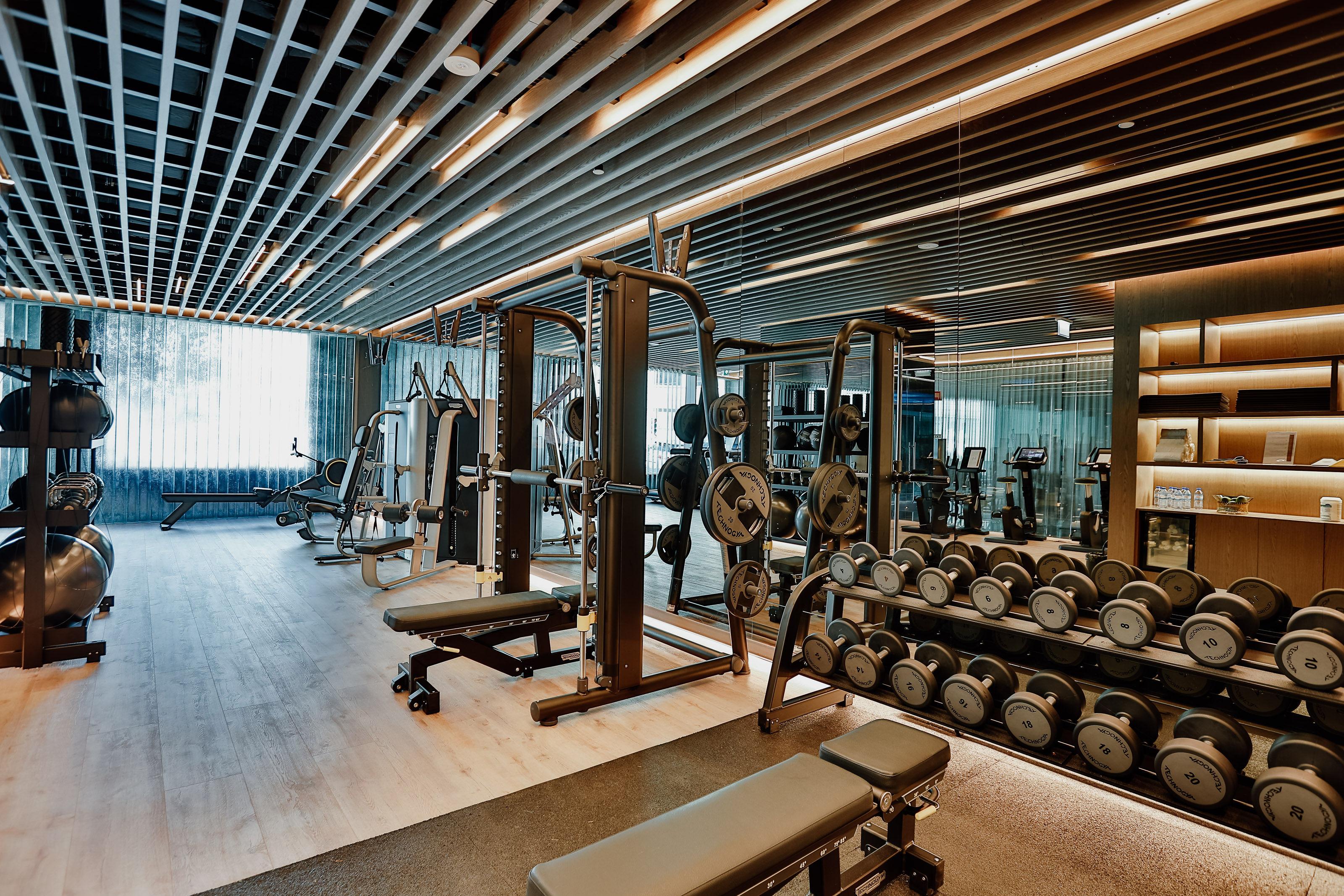 Epic Sana Marques Hotel Lissabon Exterior foto The photo shows a modern gym interior. It features various exercise equipment, including weight machines and benches. In the foreground, there is a bench for strength training, alongside a rack of dumbbells. The space has a sleek design with wooden b