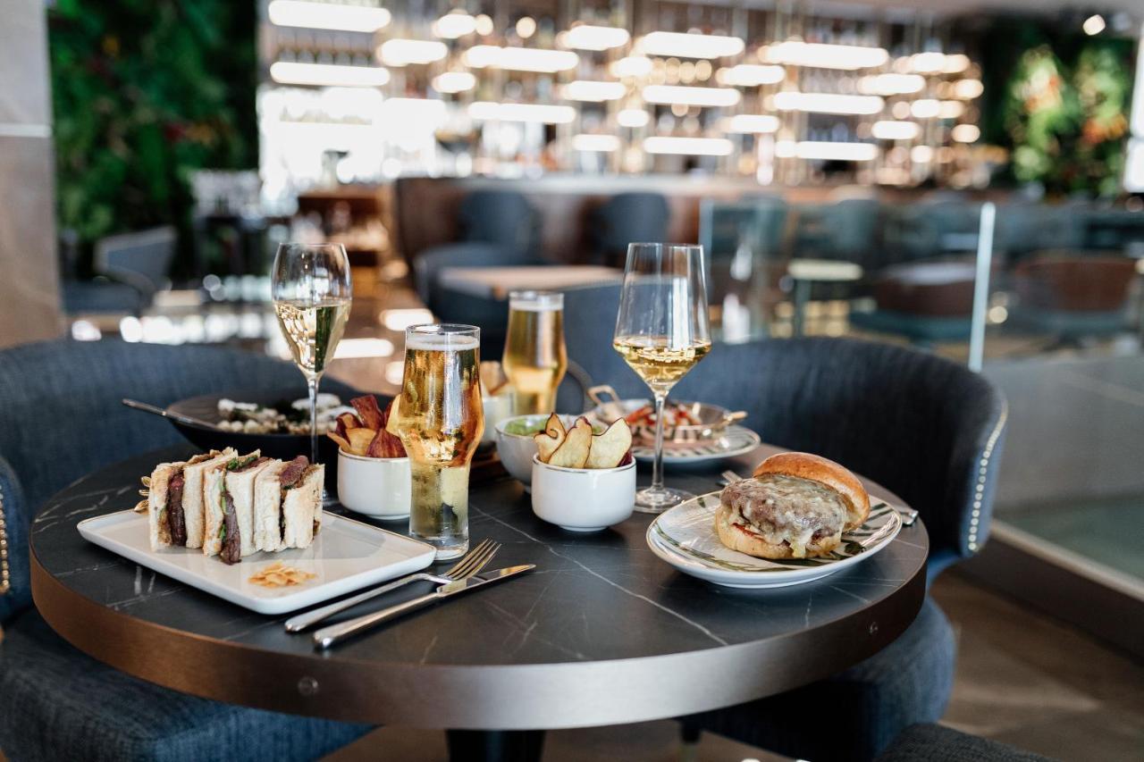 Epic Sana Marques Hotel Lissabon Exterior foto The photo shows a table set in a stylish restaurant. On the table, there are several plates of food and drinks. 

1. **Food**: 
   - There is a gourmet burger with toppings on a bun.
   - A plate of fries and possibly other sides is present.
   - A s