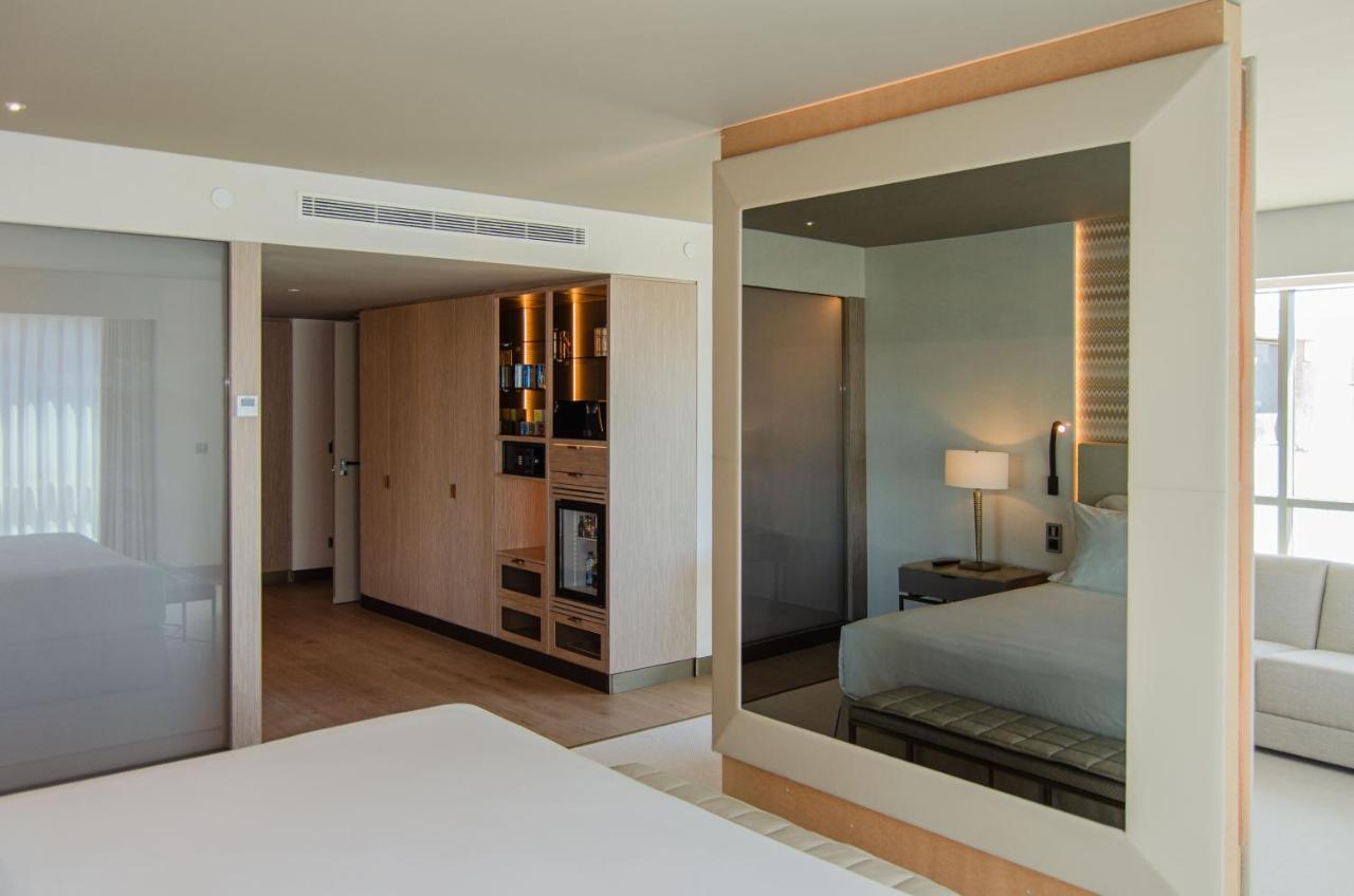 Epic Sana Marques Hotel Lissabon Exterior foto The photo shows a modern hotel room with a clean, minimalist design. In the foreground, there is a bed with a simple white bedspread. To the side, a large mirror reflects part of the room, creating an illusion of more space. Behind the bed, there is 